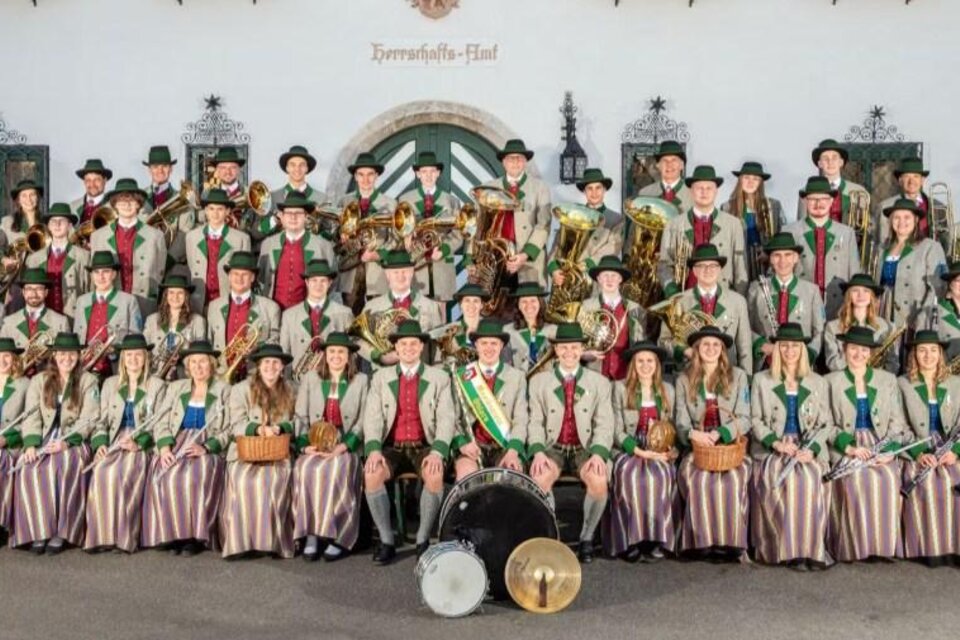Ein Musikverein tritt auf einer Bühne auf, umgeben von festlicher Dekoration. Die Musiker tragen grüne Uniformen und spielen verschiedene Instrumente. | © Musikverein Öblarn