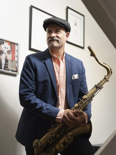 A man is standing with a saxophone in hand. He is wearing an elegant suit and smiling friendly. | © neal_sugarman_DSC2898