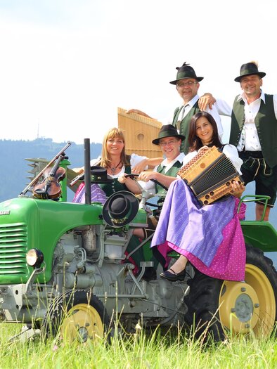 Music group in traditional costume with button accordion and other instruments on a vintage tractor at the SUMT. | © Knöpferlstreich
