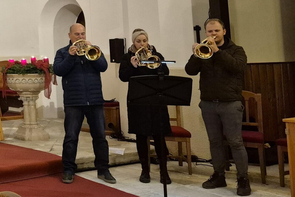 Drei Musiker spielen Trompete in einer Kirche. Sie stehen vor einem Musikständer und sind festlich gekleidet. | © g.pö