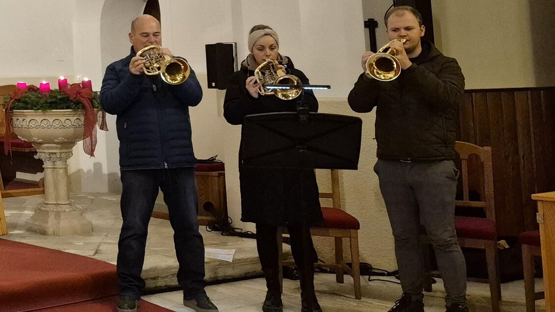 Drei Musiker spielen Trompete in einer Kirche. Sie stehen vor einem Musikständer und sind festlich gekleidet. | © g.pö