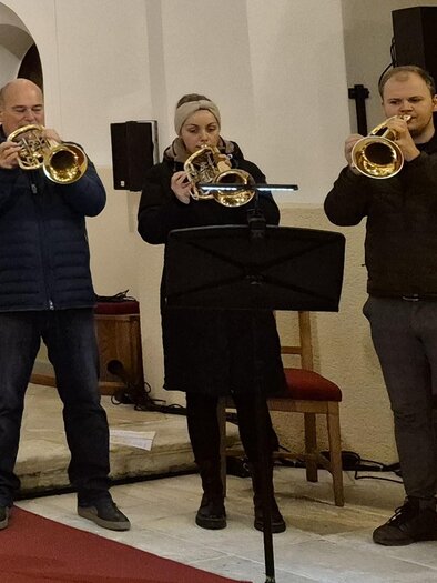 Three musicians are playing trumpet in a church. They are standing in front of a music stand and are dressed festively. | © g.pö