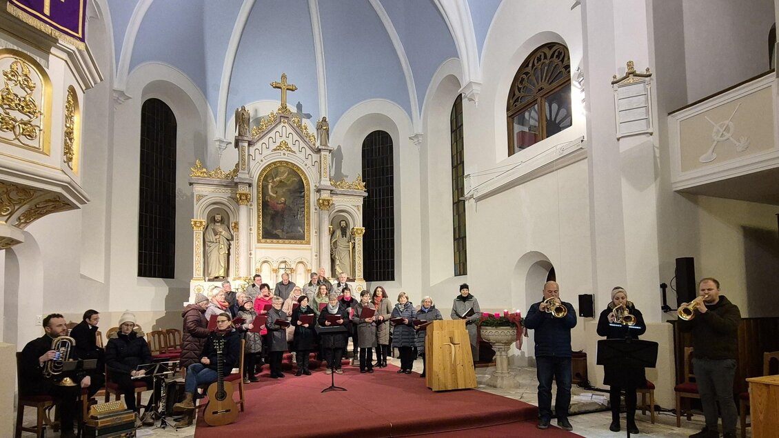 Eine Kirche mit einer bunten Gruppe von Menschen, die miteinander singen. Im Hintergrund ist ein schöner Altar zu sehen. | © g.pö