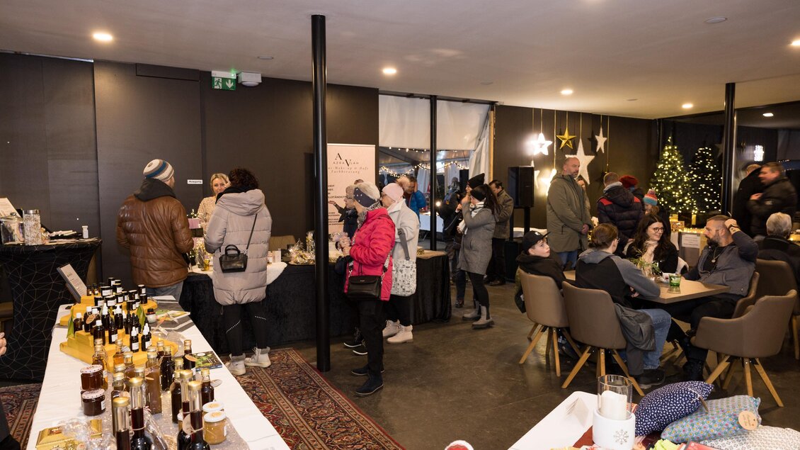 Eine festliche Veranstaltung in einem modernen Raum mit Weihnachtsdekoration. Gäste stehen an Tischen und genießen Getränke und Snacks. | © Meieregger.photos