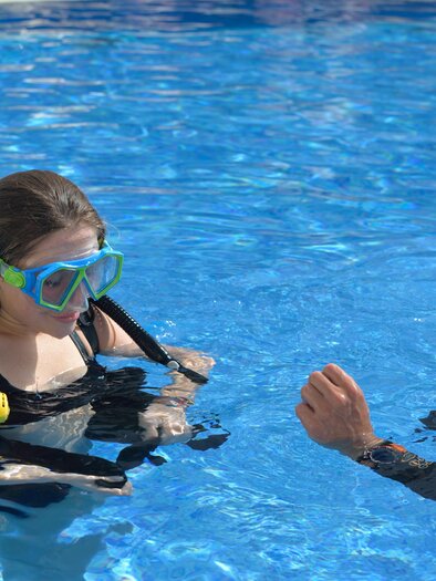 Zwei Taucher im Pool, einer im Wassertiefe mit Tauchausrüstung. Die Frau trägt eine Tauchmaske und hört dem Mann zu, der Anweisungen gibt. | © H2O-Hoteltherme GmbHiStock