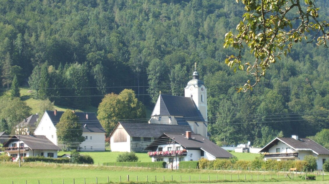 Eine malerische Landschaft mit einem kleinen Dorf und einer Kirche. Umgeben von grünen Wiesen und bewaldeten Hügeln. | © TVB Gesäuse