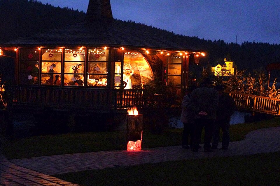 Eine beleuchtete Holzhütte in einer dämmerigen Umgebung. Menschen stehen davor und schauen hinein. | © Gemeinde Grundlsee