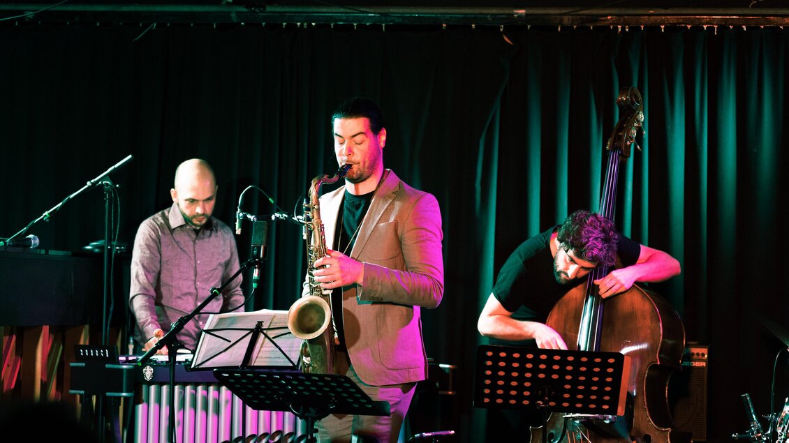Drei Musiker spielen beim Shortcut Festival in Graz Saxofon, Vibrafon und Kontrabass auf einer beleuchteten Bühne. | © Verena Pöschl