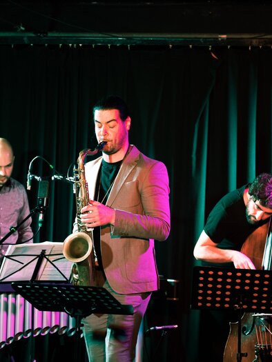Three musicians are playing saxophone, vibraphone, and double bass on a lit stage at the Shortcut Festival in Graz. | © Verena Pöschl