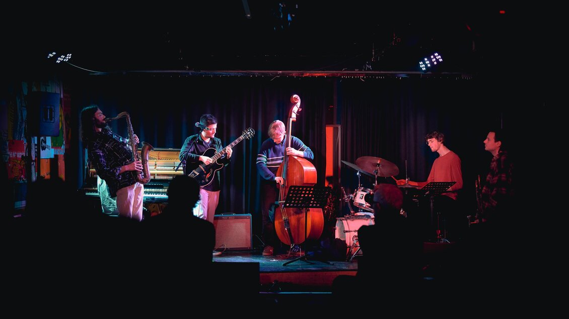 Junge Jazzmusiker spielen beim Shortcut Festival in Graz Saxofon, Gitarre, Kontrabass und Schlagzeug auf der Bühne. | © Kuro Simon