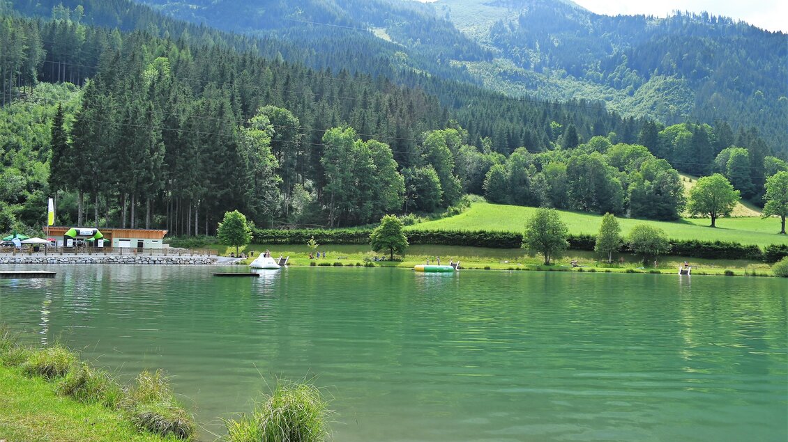 Ein malerischer See umgeben von sanften Hügeln. Die Sonne strahlt am Himmel und es gibt ein grünes, offenes Feld. | © Gem. Wald am Schoberpass