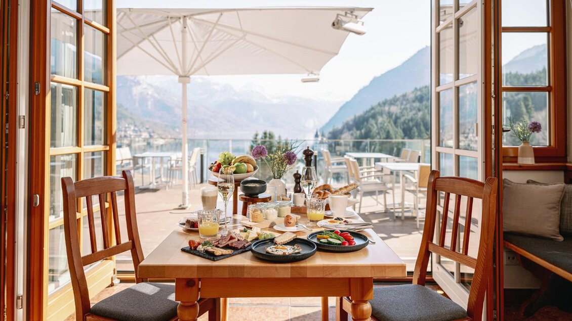 Ein schön gedeckter Tisch mit Frühstück in einem gemütlichen Raum. Große Fenster bieten einen Blick auf die Berge und die Landschaft. | © MONDI Resort Grundlsee