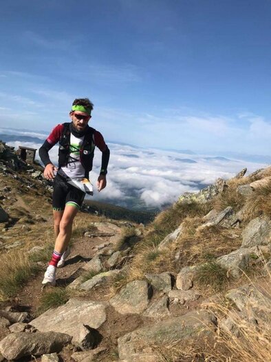 A runner moves dynamically along a rocky path in the mountains. In the background, clouds can be seen that offer an impressive view. | © Uwe Zitzenbacher