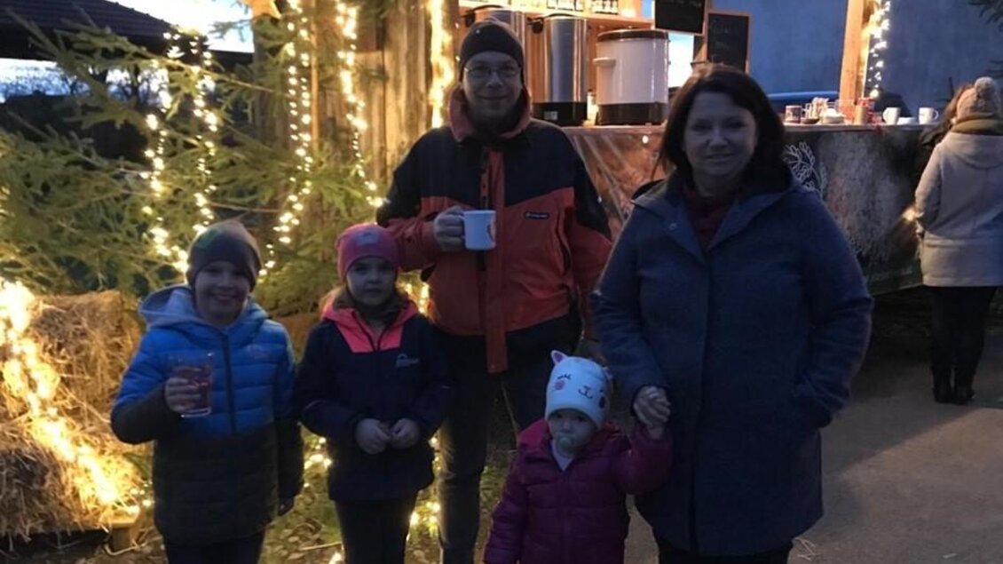 Eine Familie steht im Freien vor einem gemütlichen Stand, beleuchtet mit Lichtern. Es ist Abend und die Kinder tragen warme Kleidung. | © SteirerREIS by Fuchs