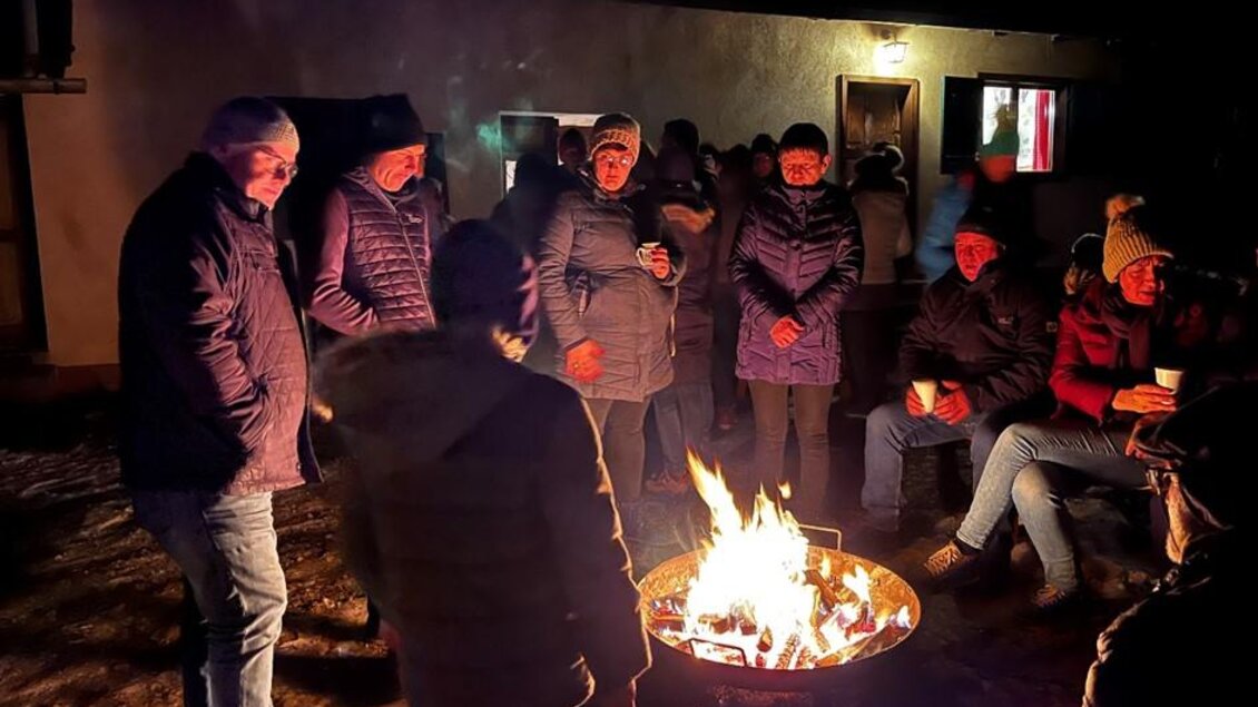 Eine Gruppe von Menschen versammelt sich rund um ein Lagerfeuer in der Dunkelheit. Sie tragen warme Kleidung und scheinen sich gut zu unterhalten. | © SteirerREIS by Fuchs