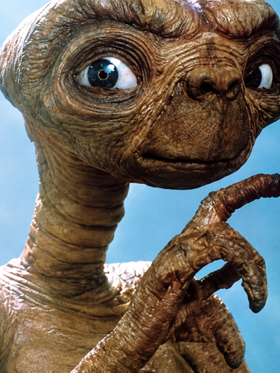 Close-up of E.T., the extraterrestrial, with large blue eyes and an raised finger with a glowing tip. | © Flimmo