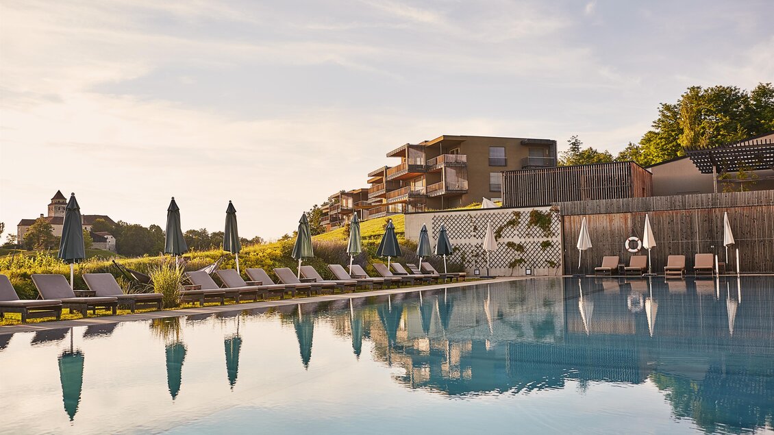 Ein eleganter Pool mit Liegen und Sonnenschirmen. Im Hintergrund sind moderne Gebäude und viel Grün zu sehen. | © LOISIUM