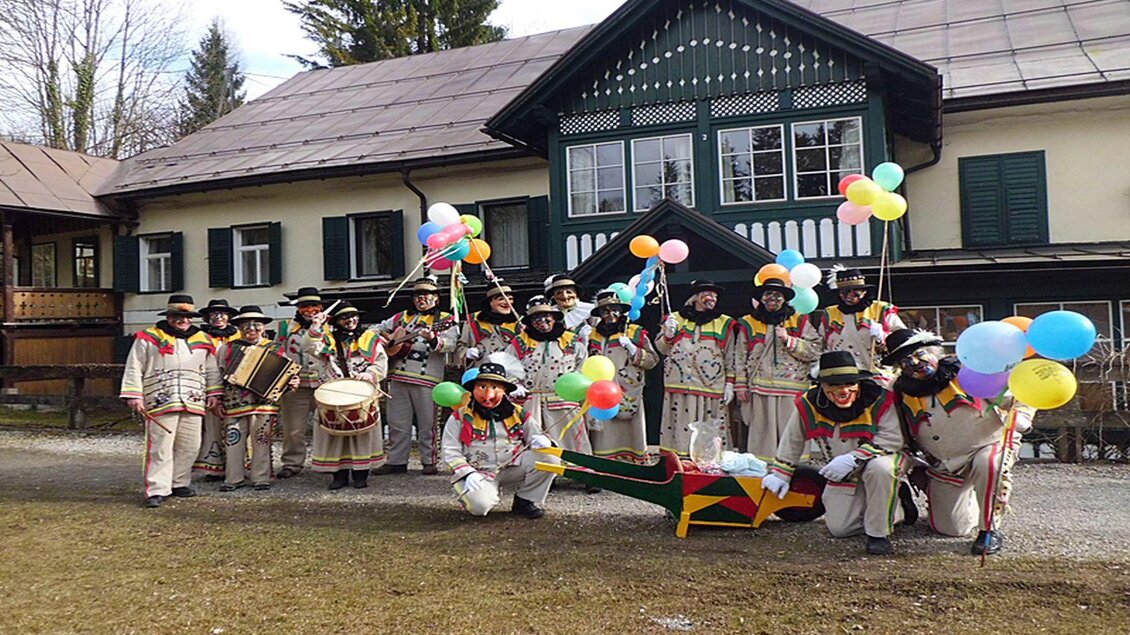 Die Gruppe der traditionell und festlich gekleideten Altausseer Knopferl steht vor einem Haus und hält bunte Ballons. Sie sind bereit für ihren Paradiestag, den höchsten Feiertag im Leben und Jahreskreis eines jeden Knopferls. | © Hermann Schröttenhamer
