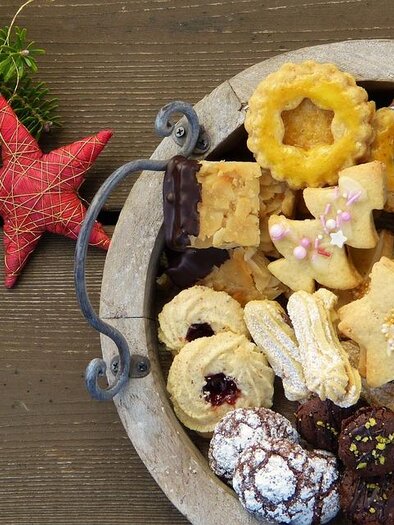 A basket full of colorful cookies and sweets, decorated with a red star and evergreen branches. The treats look festive and inviting. | © pixabay