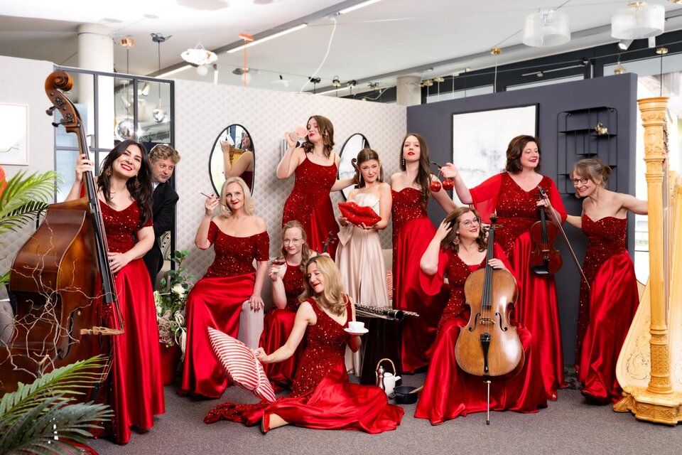 Eine Gruppe von Frauen in roten Kleidern posiert fröhlich in einem modernen Raum. Sie halten Musikinstrumente und wirken sehr ansprechend und lebhaft. | © Michaela Begsteiger