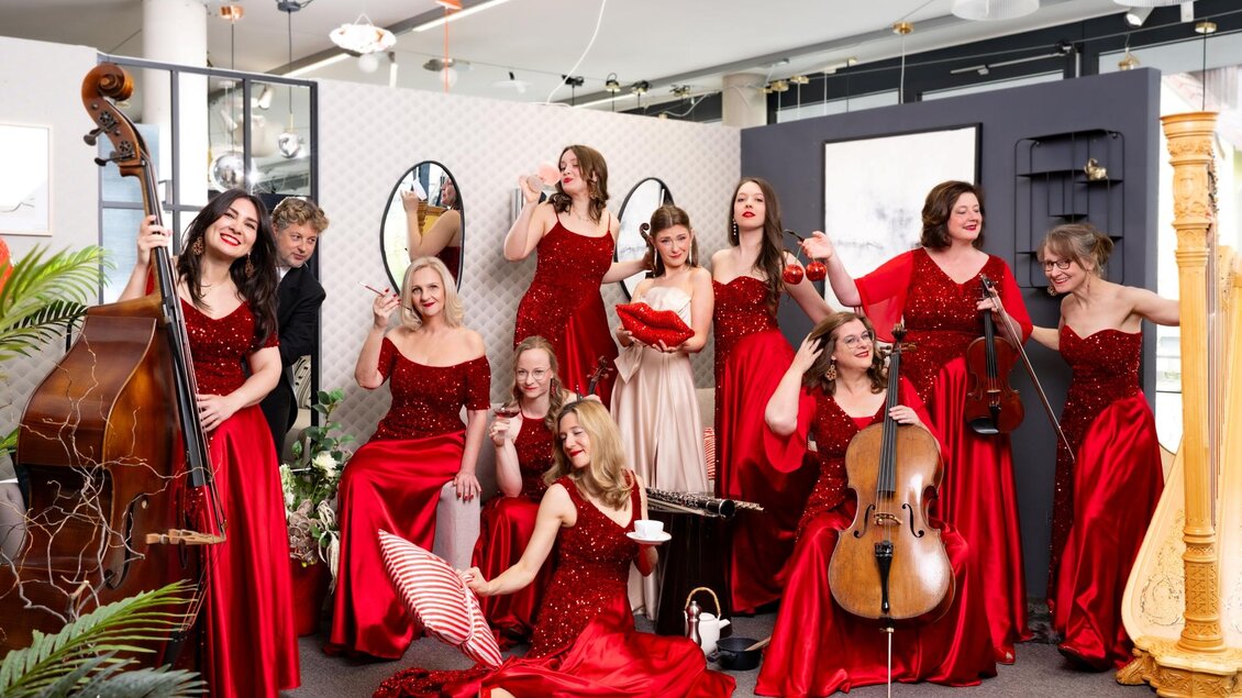 Eine Gruppe von Frauen in roten Kleidern posiert fröhlich in einem modernen Raum. Sie halten Musikinstrumente und wirken sehr ansprechend und lebhaft. | © Michaela Begsteiger