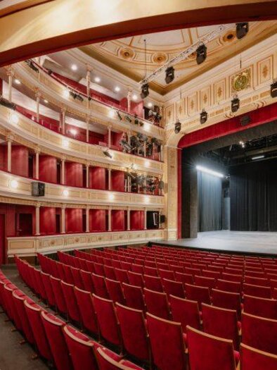 An elegant theater with red seats and a large stage. The curved architecture and decorative details create an inviting atmosphere. | © Lex Karelly