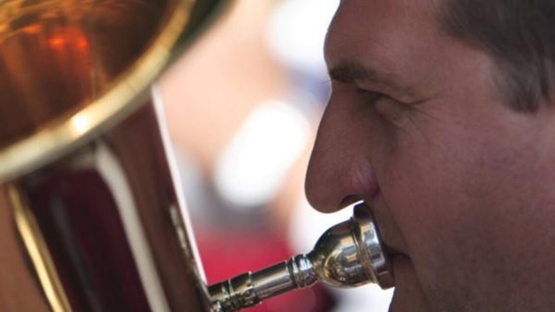 Ein Musiker spielt eine Tuba. Sein Gesicht ist nah am Instrument, während er konzentriert musiziert.
