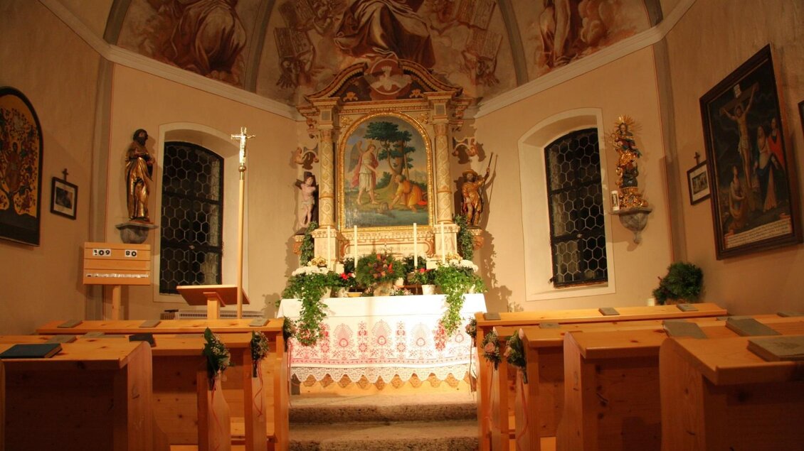 Eine kleine Kapelle mit einem kunstvoll gestalteten Altar. Die Bänke sind aus Holz und die Wände sind mit historischen Gemälden verziert. | © Mares Rastl