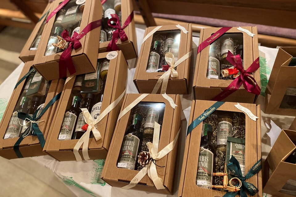 Mehrere Geschenkboxen mit Flaschen in verschiedenen Verpackungen sind auf einem Tisch angeordnet. Jede Box ist mit einer dekorativen Schleife geschmückt. | © Hofladen Hauptmann