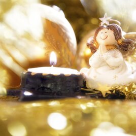 Porcelain angel sits with folded hands in front of a burning tea light with a smile on its face, background gold lametta. | © Steiermark Tourismus-photostyle.at