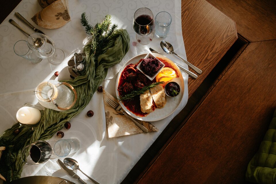 Ein schön gedeckter Tisch mit einem Teller, der verschiedene Arten von Essen, darunter Fleisch und Obst, zeigt. Um den Teller herum stehen Gläser und Besteck, was eine festliche Atmosphäre schafft. | © Studio-draussen