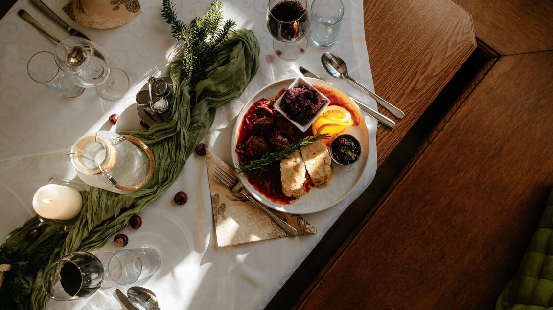 Ein schön gedeckter Tisch mit einem Teller, der verschiedene Arten von Essen, darunter Fleisch und Obst, zeigt. Um den Teller herum stehen Gläser und Besteck, was eine festliche Atmosphäre schafft. | © Studio-draussen