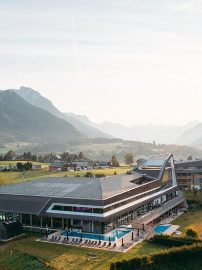 Ein modernes Gebäude in der Natur, umgeben von Bergen und Wiesen. Der Poolbereich ist gut sichtbar und die Landschaft strahlt Ruhe aus. | © Karl Steinegger
