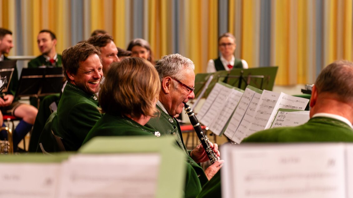 Eine Gruppe von Musikern in traditionellen Trachten spielt zusammen auf einer Bühne. Die Stimmung ist fröhlich und entspannt, während sie ihre Instrumente betrachten. | © David Stocker