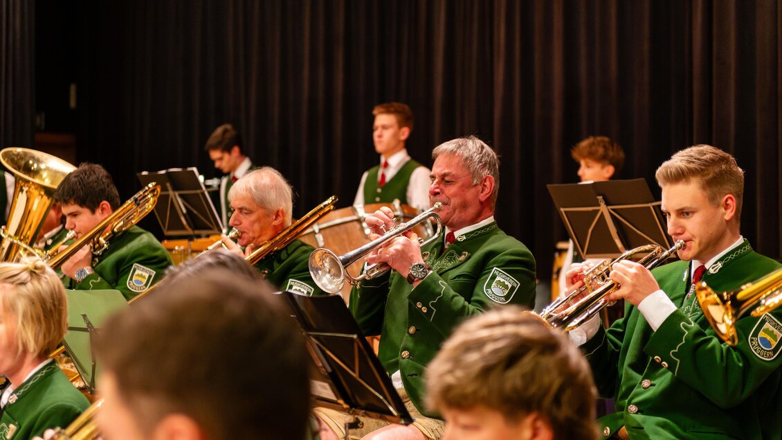 Eine Musikgruppe spielt auf der Bühne und trägt grüne Uniformen. Sie spielen verschiedene Blasinstrumente in einem festlichen Ambiente. | © David Stocker