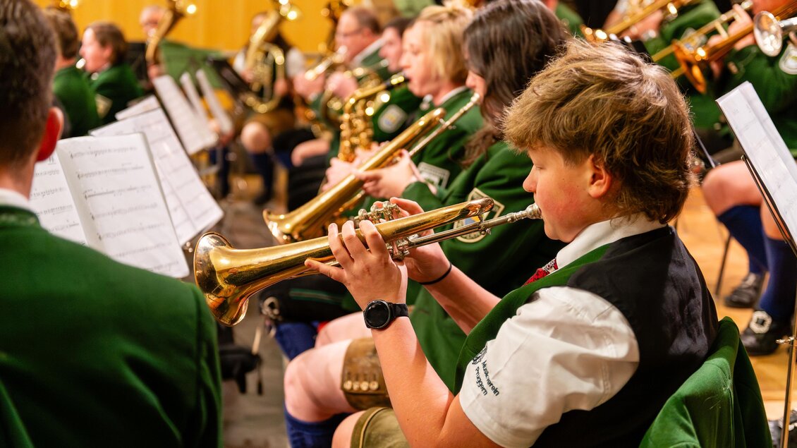 Ein Jugendlicher spielt Trompete in einem Blasorchester. Die Musiker tragen grüne Uniformen und konzentrieren sich auf ihre Instrumente. | © David Stocker