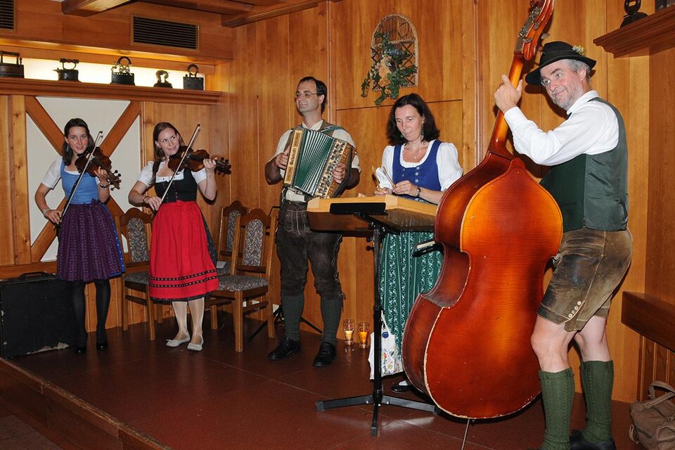 Eine musikalische Gruppe spielt traditionelle Instrumente in einer gemütlichen Holzstube. Die Künstler sind in festlicher Tracht gekleidet. | © Simon Mühle