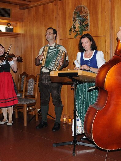 Eine musikalische Gruppe spielt traditionelle Instrumente in einer gemütlichen Holzstube. Die Künstler sind in festlicher Tracht gekleidet. | © Simon Mühle