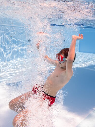Ein Junge taucht im Schwimmbad und erzeugt Spritzer. Er trägt eine Taucherbrille und genießt das Wasser. | © H2O-Hoteltherme GmbHmoving.stills
