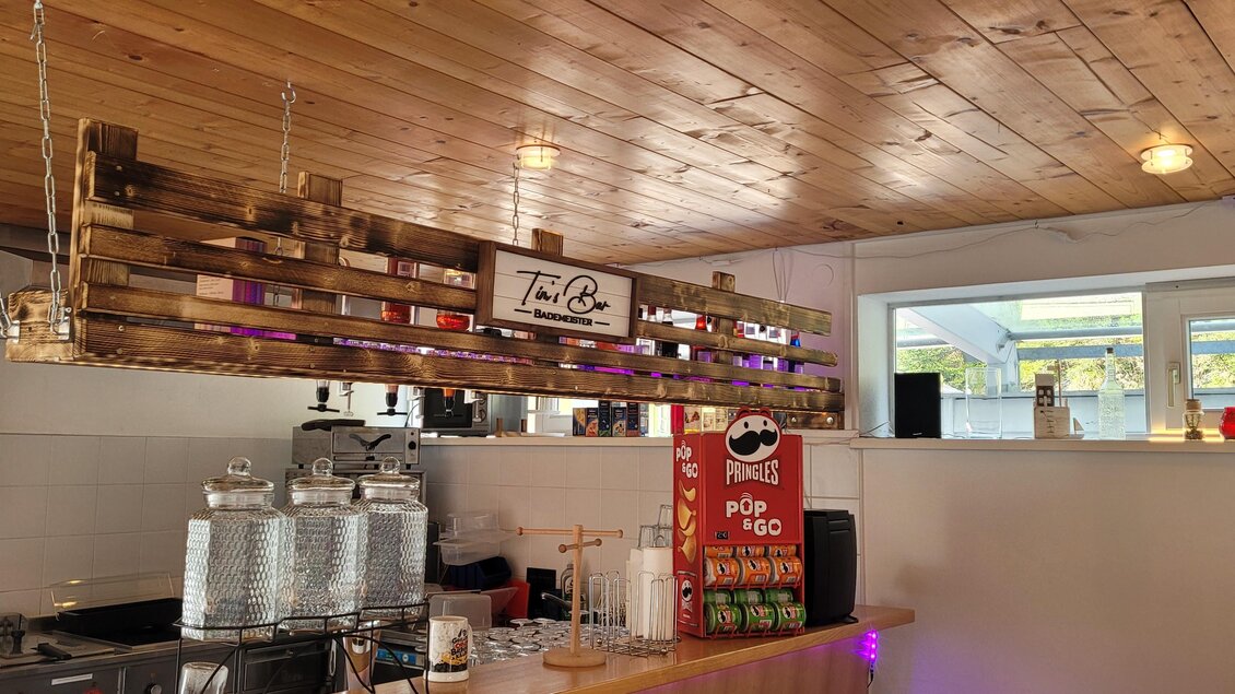 Ein gemütliches Café mit Holzwänden und modernen Möbeln. Die Theke ist mit Getränken und einer dekorativen Holzleiste ausgestattet. | © Tim Fuchsberger 