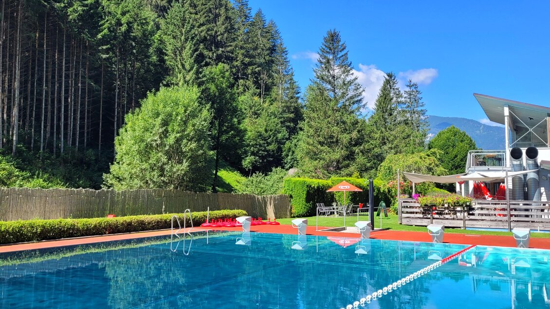Ein schöner Pool umgeben von Bäumen und gepflegten Grünflächen. Strahlend blauer Himmel sorgt für eine einladende Atmosphäre. | © Tim Fuchsberger 