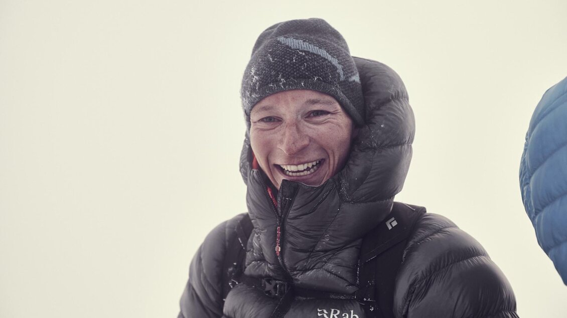 Eine lächelnde Person trägt eine warme Jacke und eine Mütze. Im Hintergrund ist eine neblige, kalte Umgebung sichtbar. | © Roman Mayerl