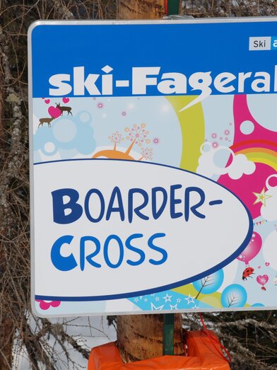 Ein bunter Hinweis auf den Boardercross-Bereich in der Ski-Fageralm. Die Grafik enthält farbenfrohe Elemente und den Namen der Ski-Region.