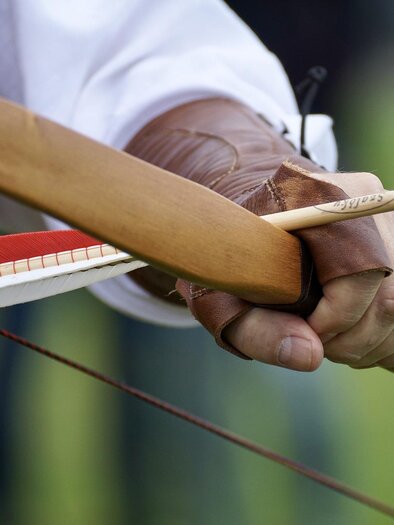 A bow is drawn, with an arrow in the archer's hand. The background shows a green meadow. | © Symbolfoto Pixabay