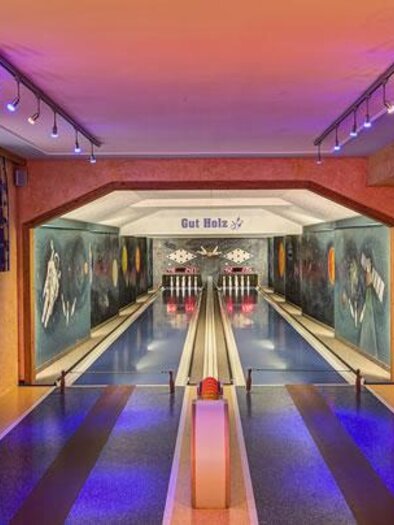 A modern bowling alley with colorful lights and stylish wall murals. The space is elegantly designed and invites you to play. | © Brückenhof Ramsau am Dachstein