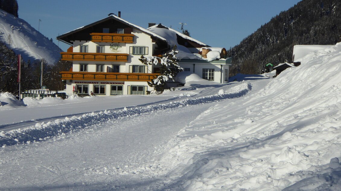 Ein charmantes Gebäude im Schnee, umgeben von malerischen Bergen. Die Landschaft ist winterlich und einladend.