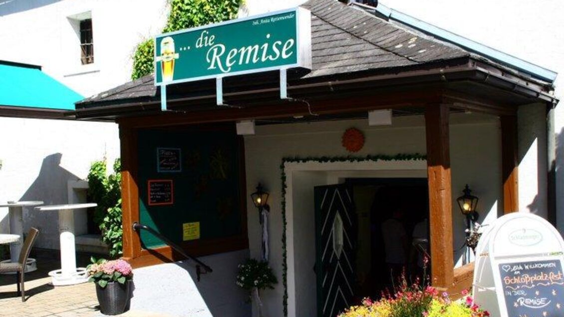 Ein einladender Eingang zu einem Restaurant namens "die Remise". Der Bereich ist mit bunten Blumen und einer Tafel dekoriert. | © Remise