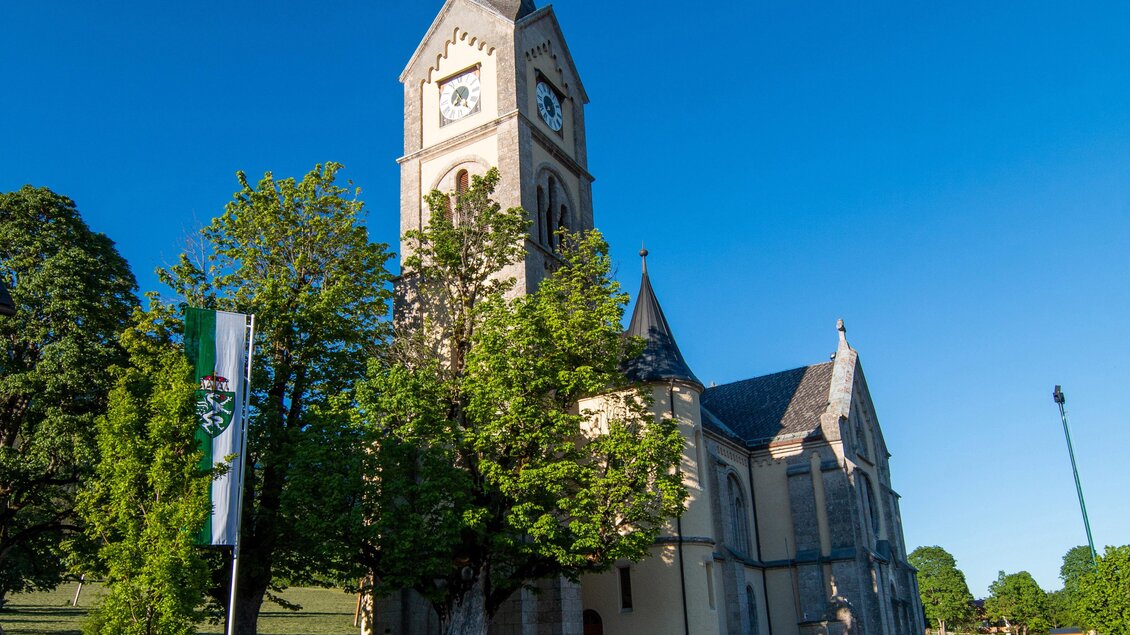 Eine malerische Kirche mit einem hohen Turm und umgeben von Bäumen. Der klare blaue Himmel ergänzt die friedliche Atmosphäre. | © photo-austria.at/Hans Simonlehner