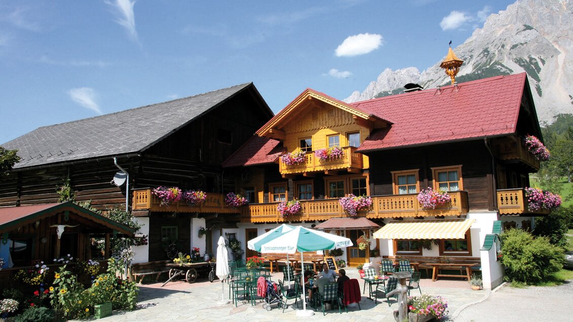 Ein charmantes alpenländisches Haus mit bunten Blumen und einem gemütlichen Außenbereich. Im Hintergrund sind majestätische Berge zu sehen. | © Ederhof
