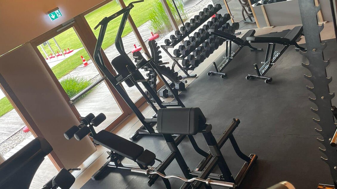 Ein modernes Fitnessstudio mit verschiedenen Trainingsgeräten. Die großen Fenster sorgen für viel Tageslicht und einen Blick ins Freie.